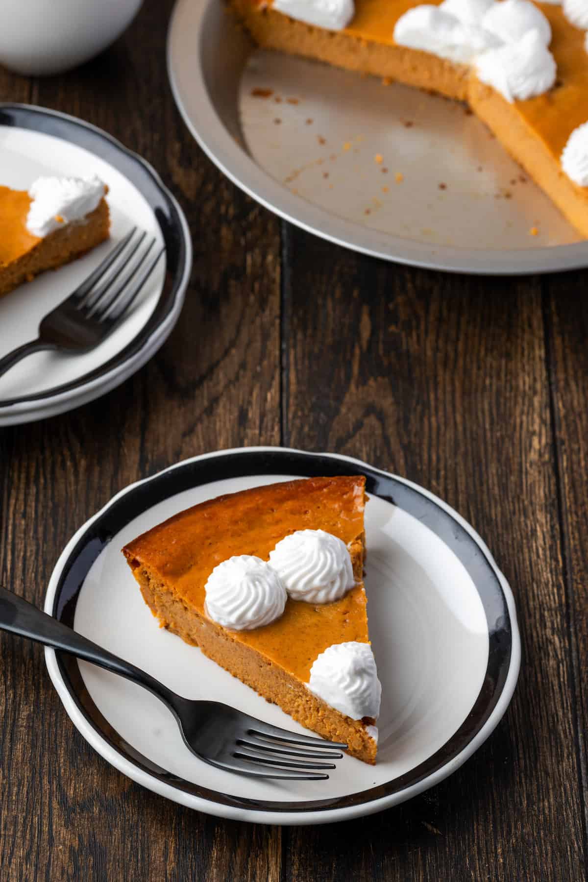 A slice of crustless pumpkin pie on a plate with a fork, with the rest of the pie in the bakground.