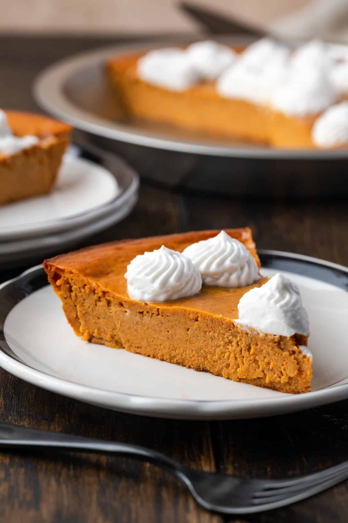 A slice of crustless pumpkin pie on a plate with a fork, with the rest of the pie in the bakground.