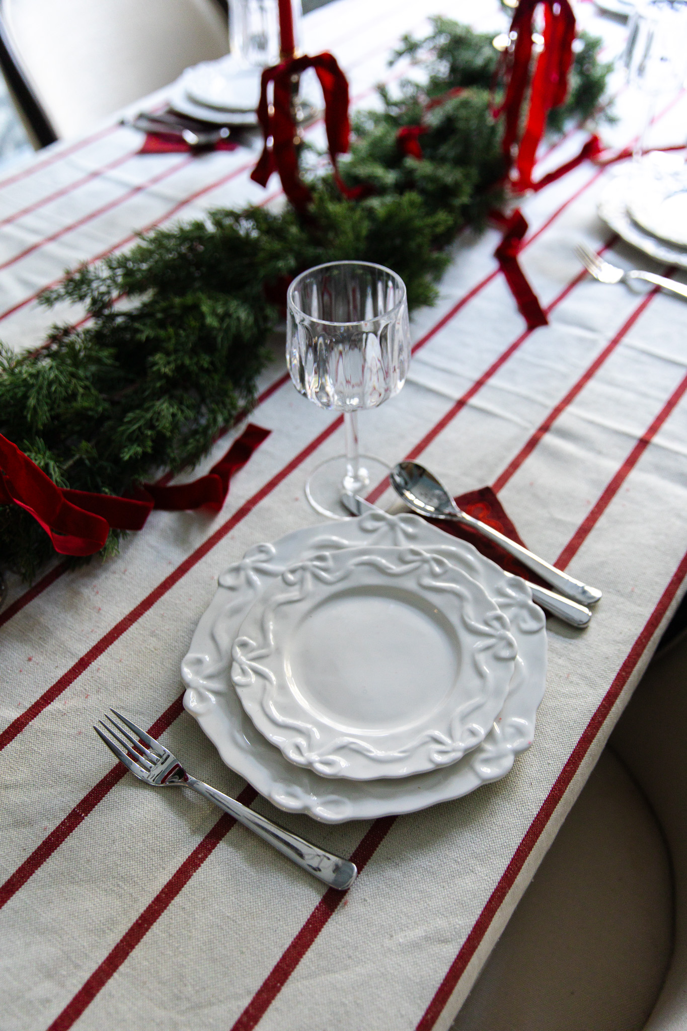 A close-up of a place setting with ceramic bow-trimmed plates, red napkins, and a red-striped tablecloth