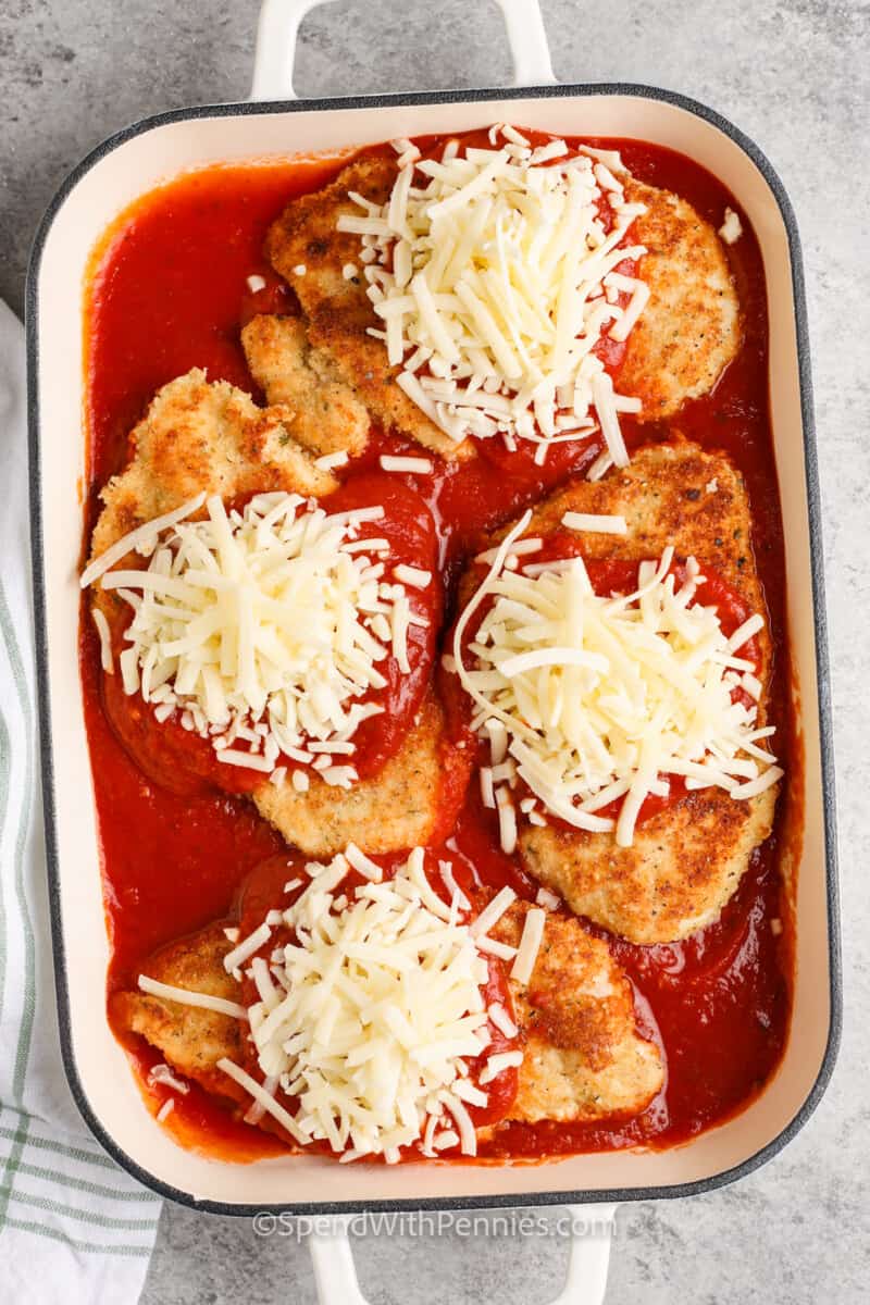 adding cheese and sauce to chicken to make Easy Chicken Parmesan