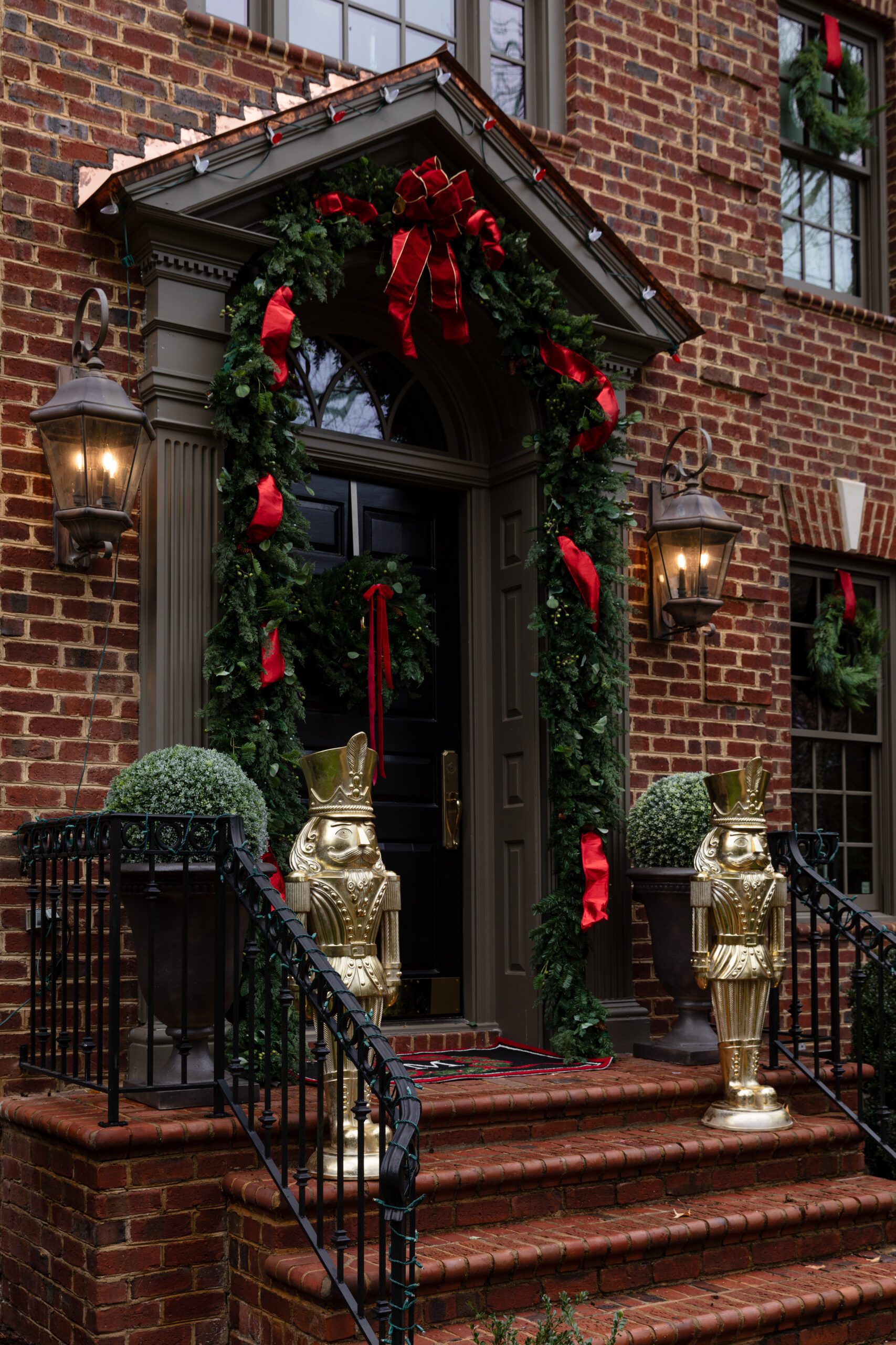 The front door of a brick home decorated for Christmas with traditional green and red colors