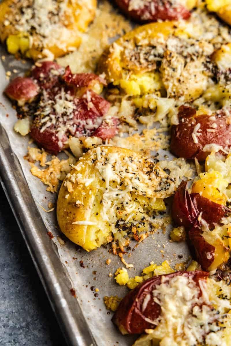 A close up of a sheet pan holding golden brown cheesy garlic bread smashed potatoes.