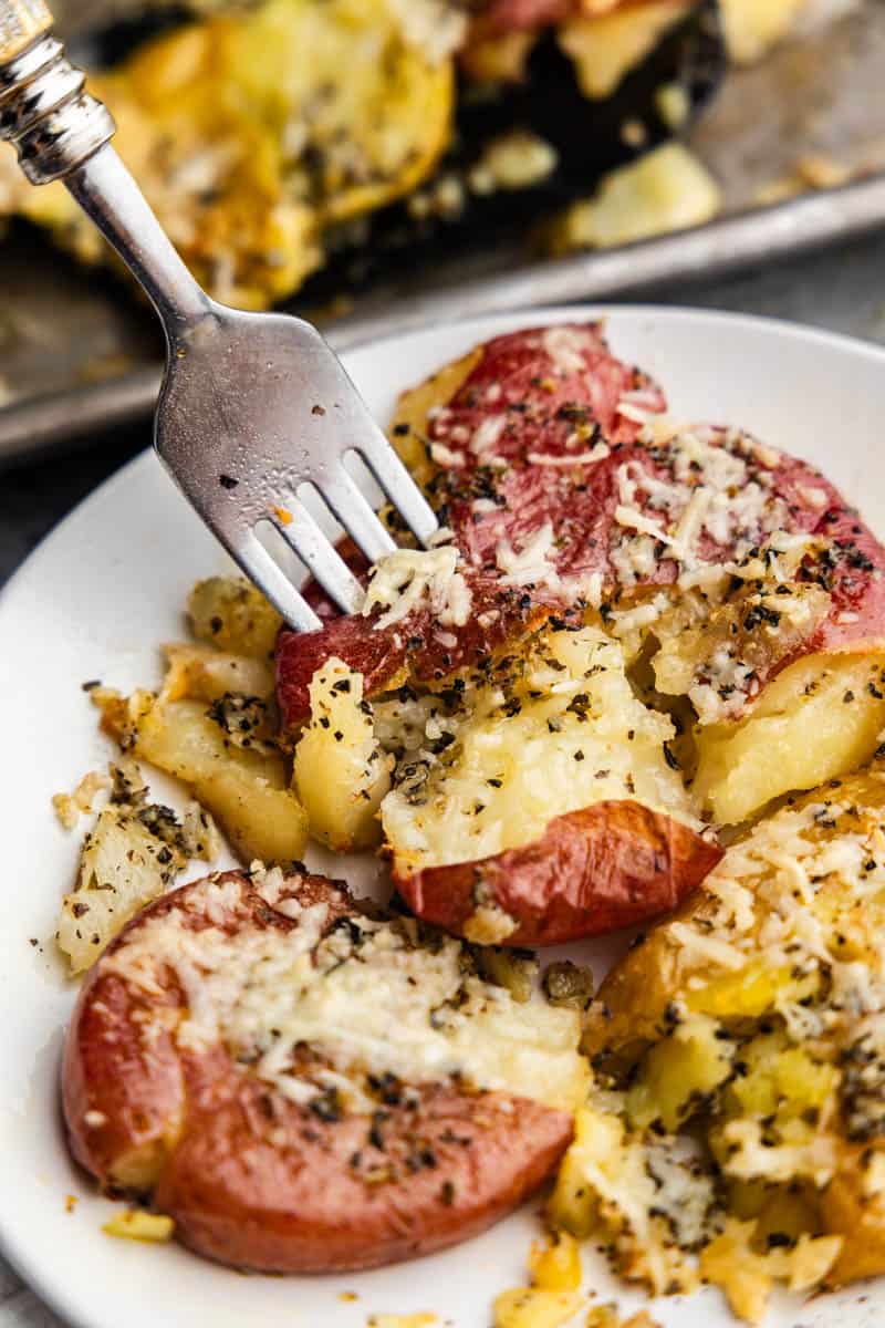 A close up of a fork spearing into a serving of garlic bread smashed potatoes for a bite.