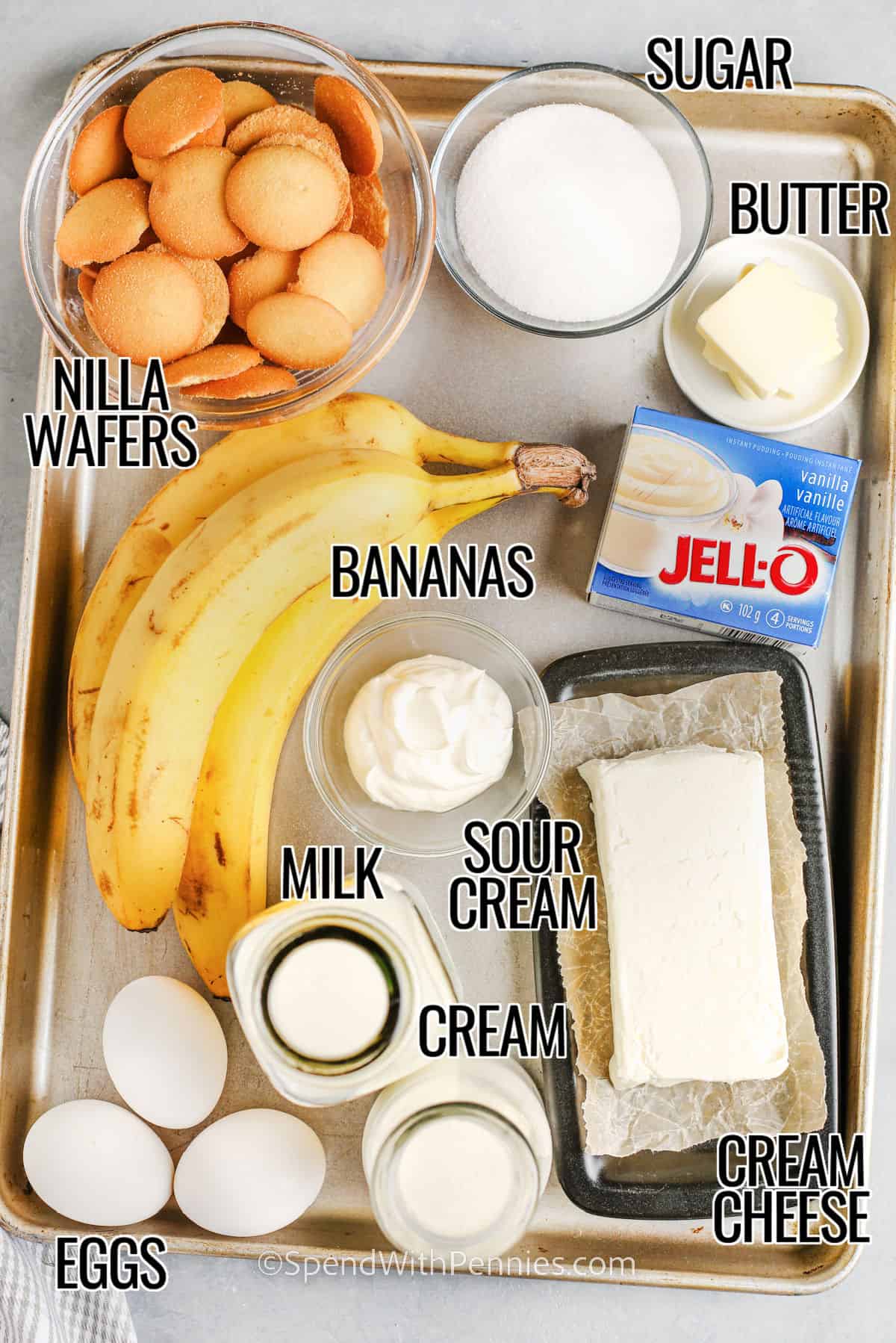 ingredients to make banana pudding cheesecake including nilla wafers, sugar, butter, bananas, pudding mix, sour cream, cream cheese, cream, milk, and eggs