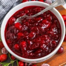 white bowl with Quick Citrus Cranberry Sauce and a spoon with cranberries around the bowl