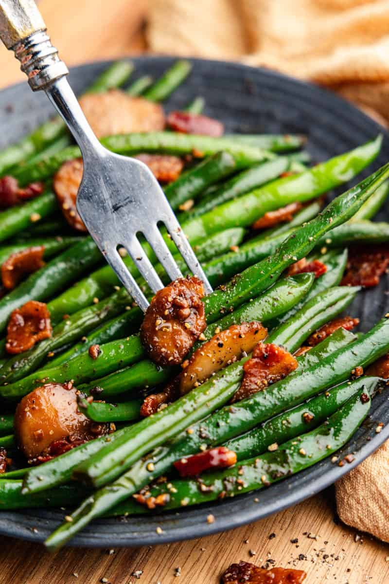 fork on plate of sauteed green beans with bacon and water chestnuts