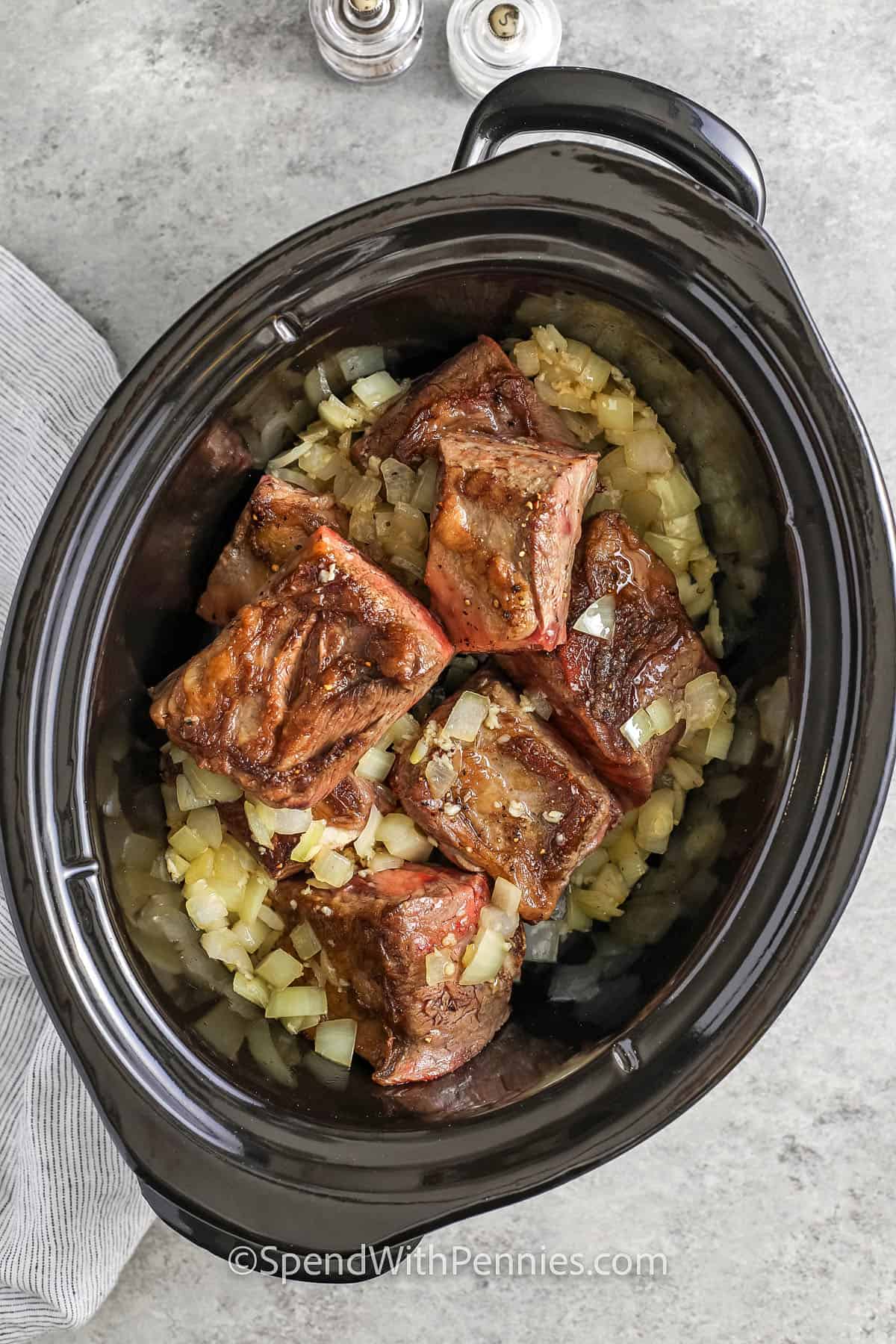 adding cooked onions and ribs to crockpot to make Slow Cooker Short Ribs