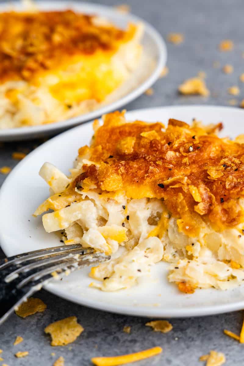 A white plate with a serving of funeral potatoes on it. A fork is resting on the plate as if a bite has just been taken from it.