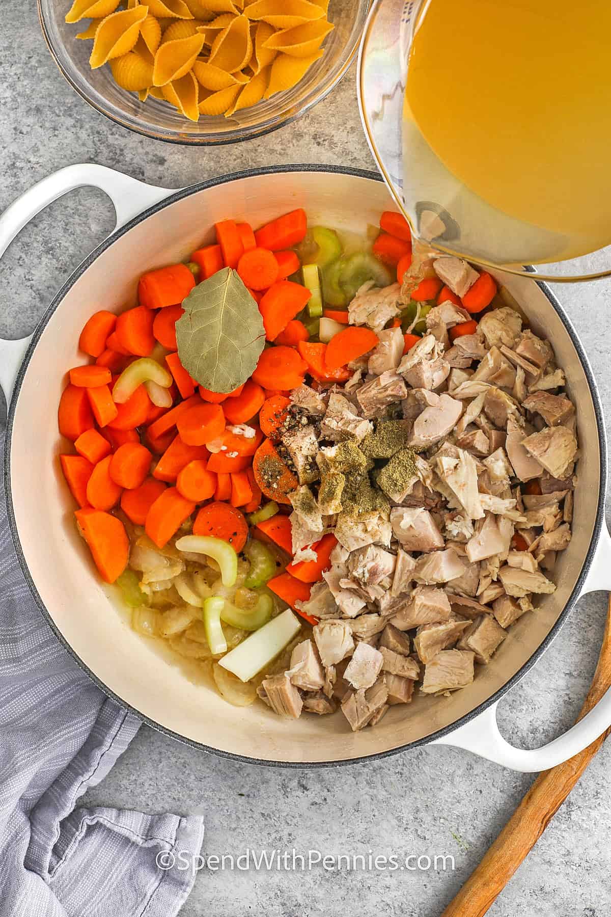 adding broth to vegetables and turkey in a Dutch oven for turkey soup