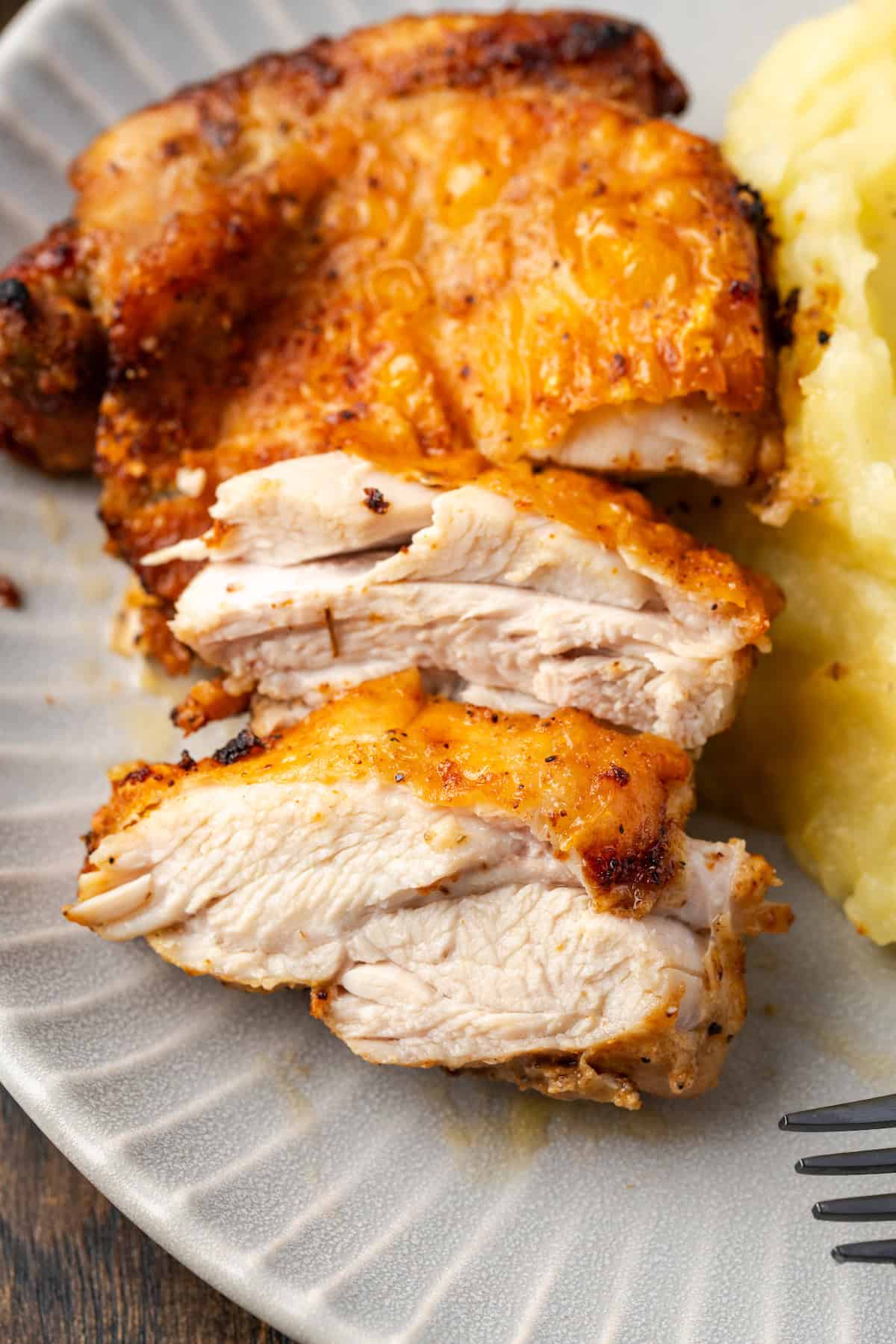 Close up of a chicken thigh cut into slices next to mashed potatoes on a plate.