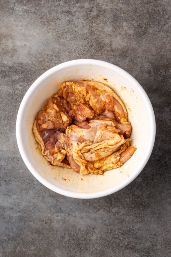 Chicken thighs covered in seasoning in a large bowl.