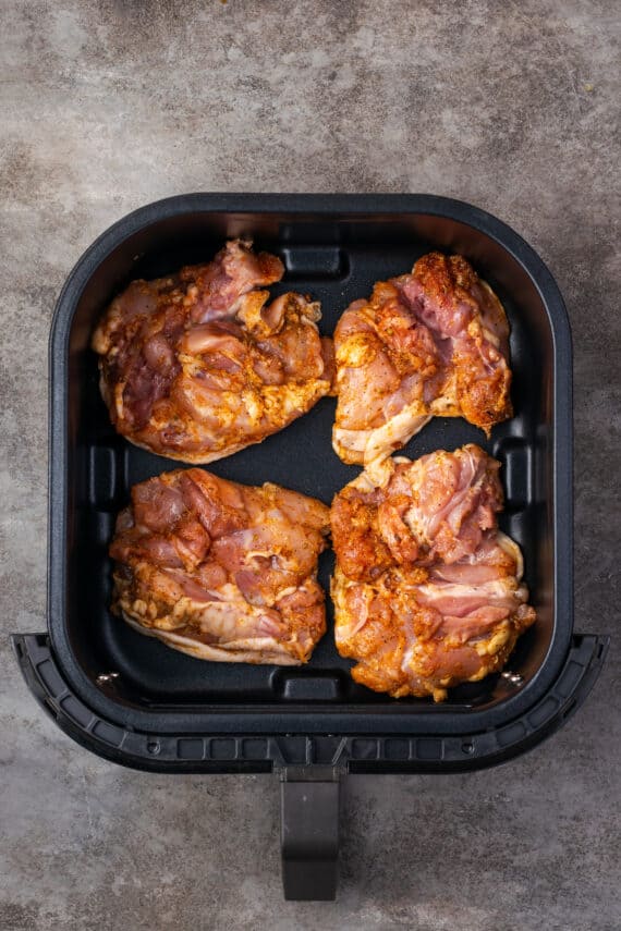 Four seasoned uncooked chicken thighs arranged inside the air fryer.