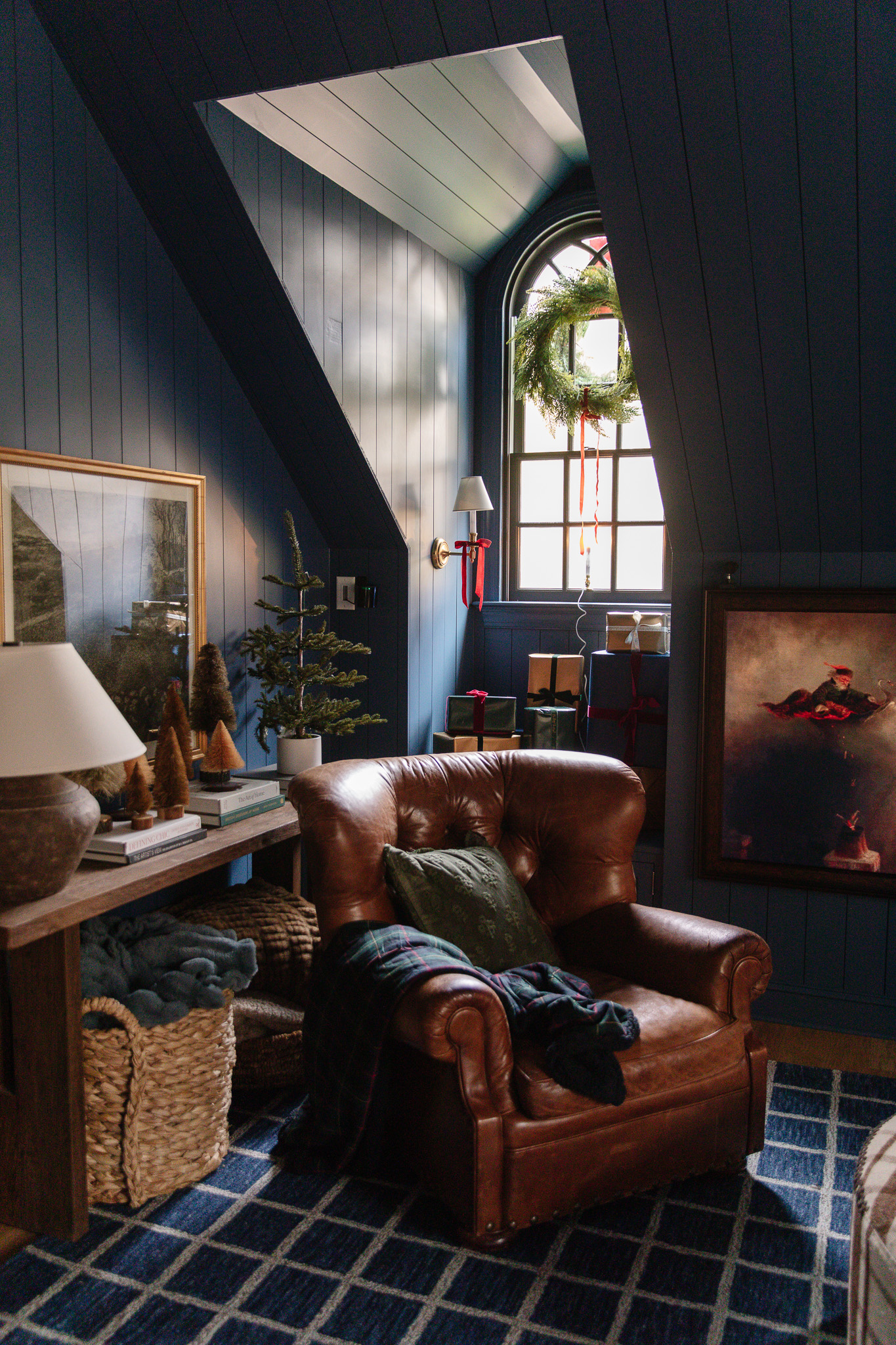 A nook of the blue bonus room with a leather chair, a red bow on the sconce, and a classic wreath inside the window