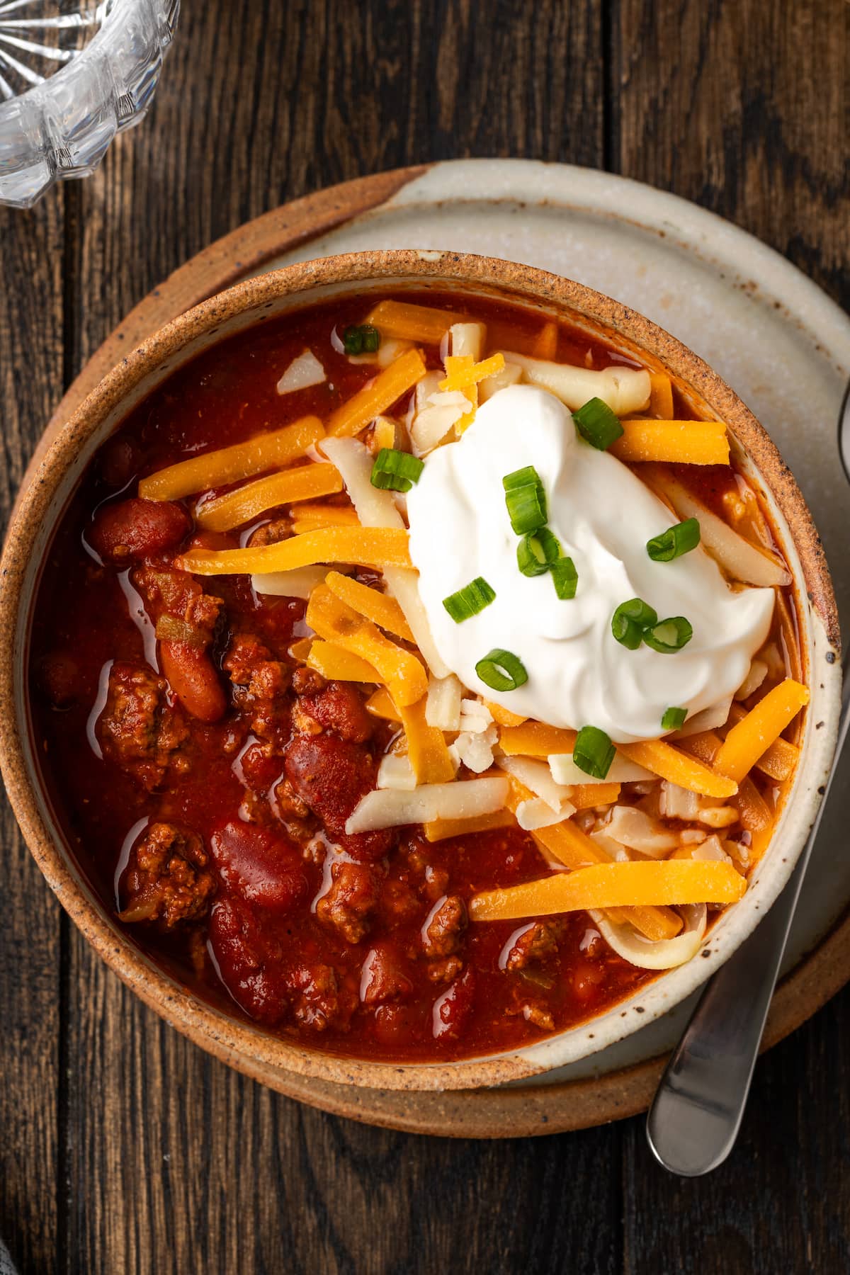 Overhead view of instant pot chili garnished with shredded cheese, sour cream, and chives in a stoneware bowl.