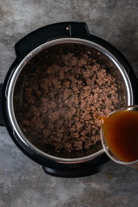 Beef broth is poured over browned ground meat in the instant pot.