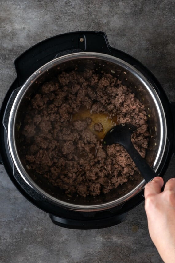 A hand uses a plastic stirring spoon to deglaze the bottom of the instant pot.