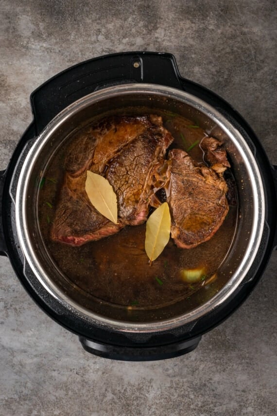 Chuck roast covered with stock and two bay leaves inside the instant pot.