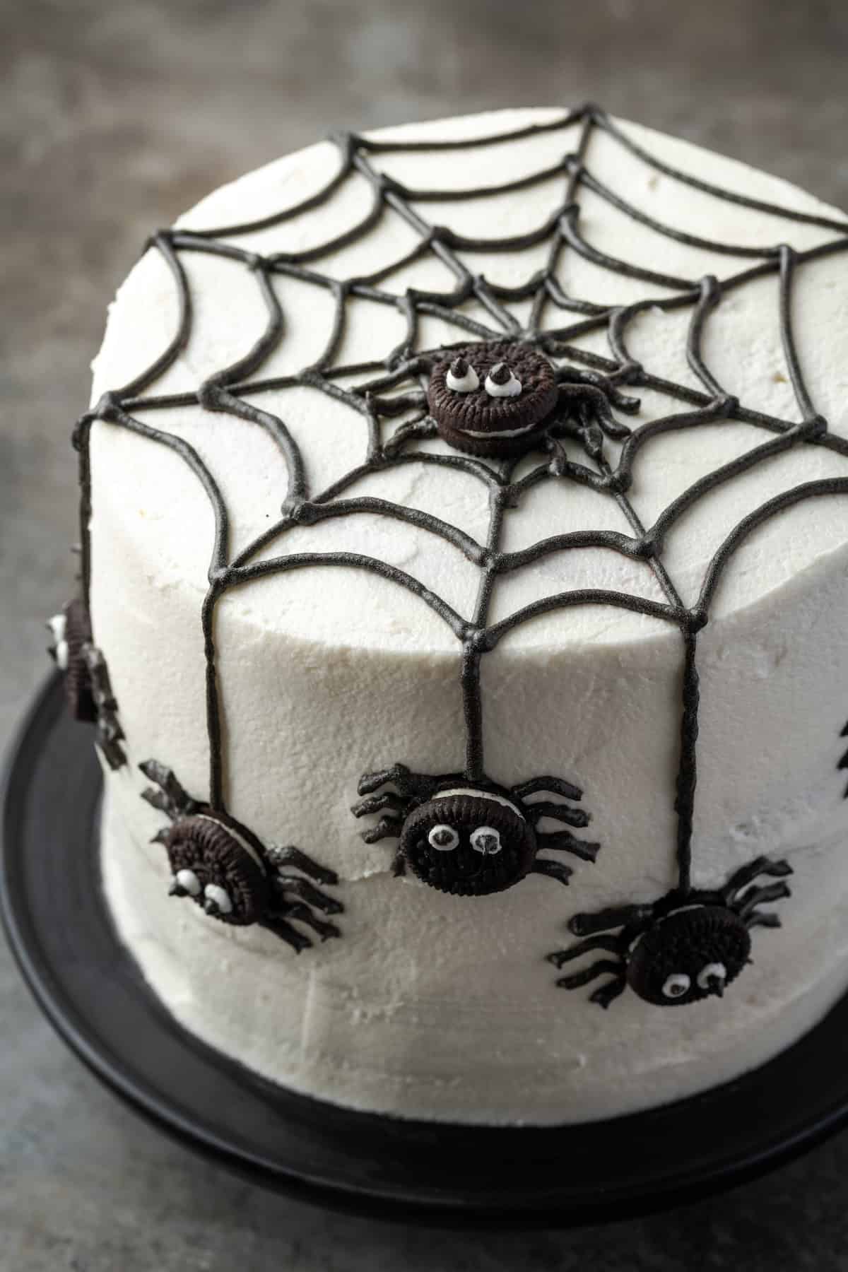 A spider cake topped with a black frosting web and mini Oreos decorated to look like spiders.