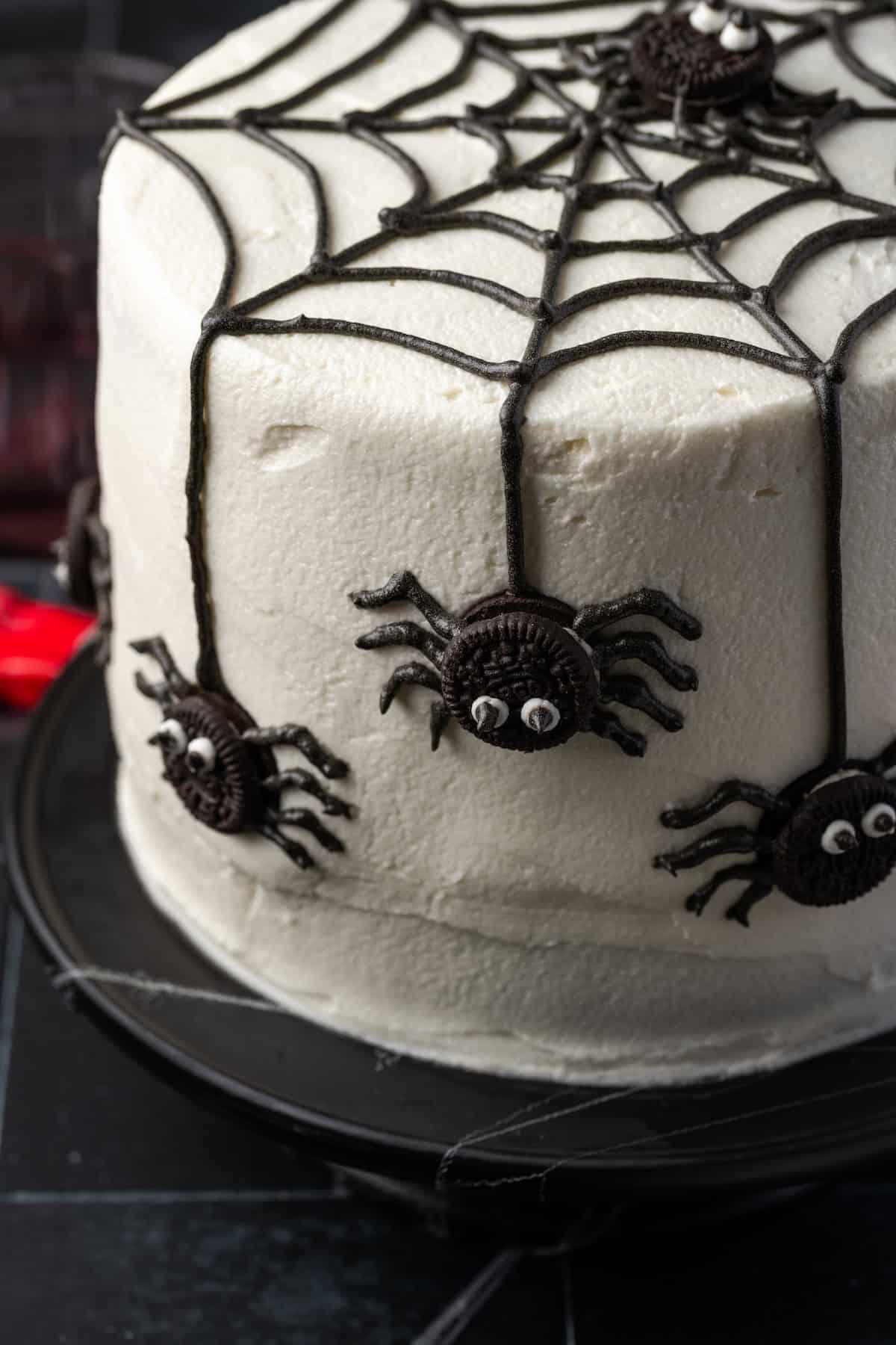 A spider cake topped with a black frosting web and mini Oreos decorated to look like spiders.