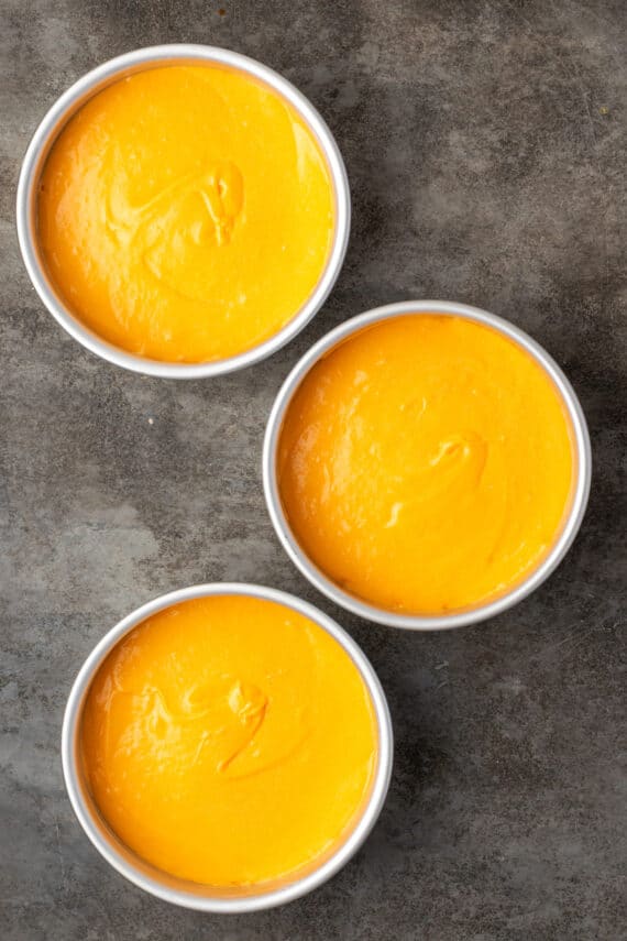 Overhead view of three cake pans filled with orange cake batter.