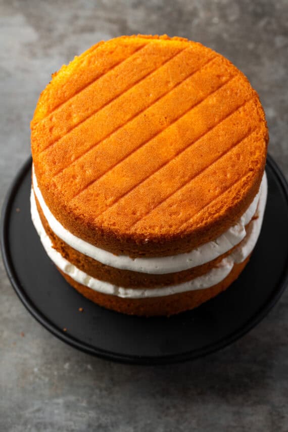 Three orange cake layers stacked with vanilla buttercream frosting piped in between each layer.