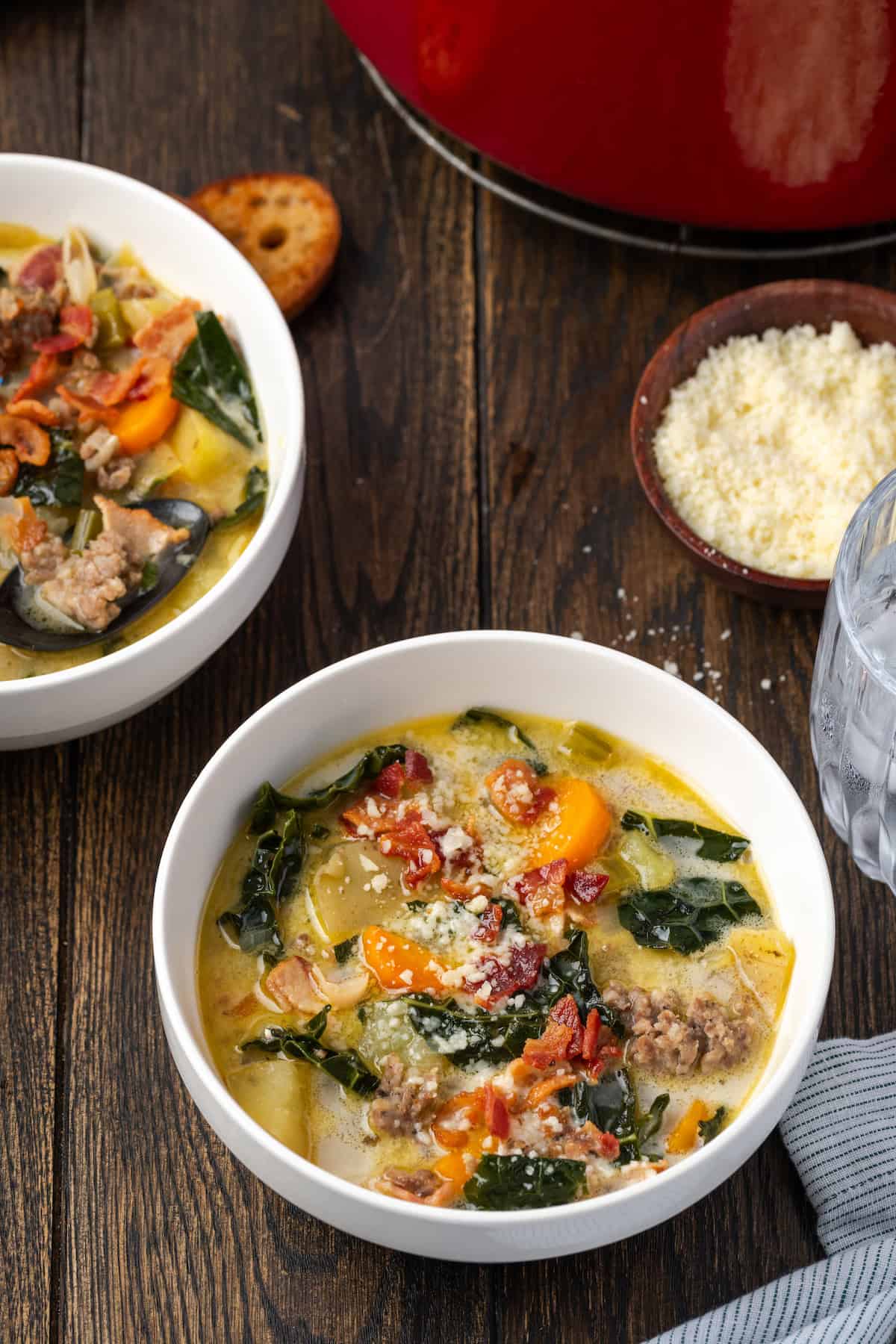 Two bowls of Zuppa Toscana next to a bowl of grated parmesan cheese.