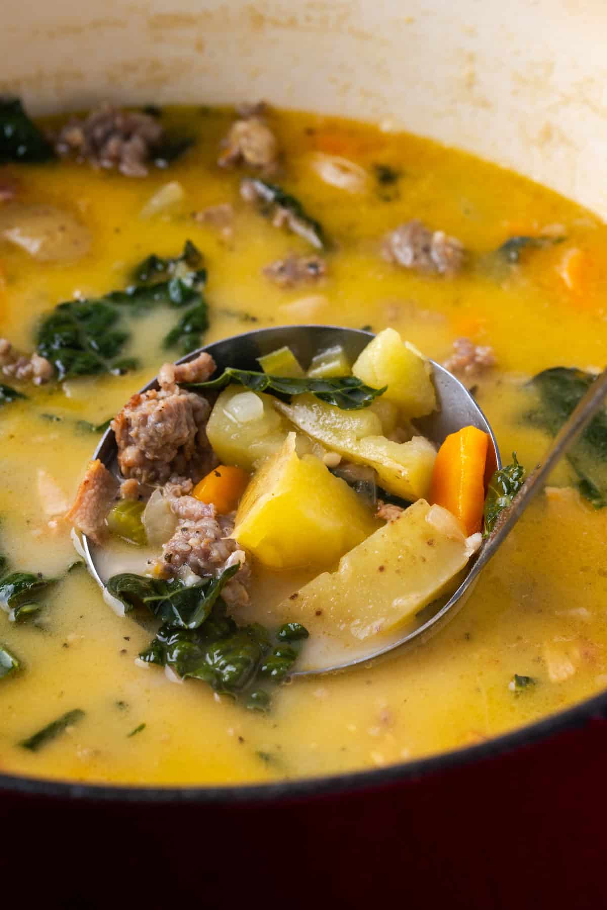 A ladle lifting Zuppa Toscana from a pot.