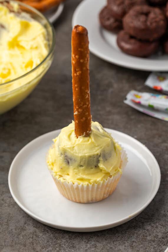 A cupcake topped with a mini donut covered with frosting, creating the base for a broom shape.