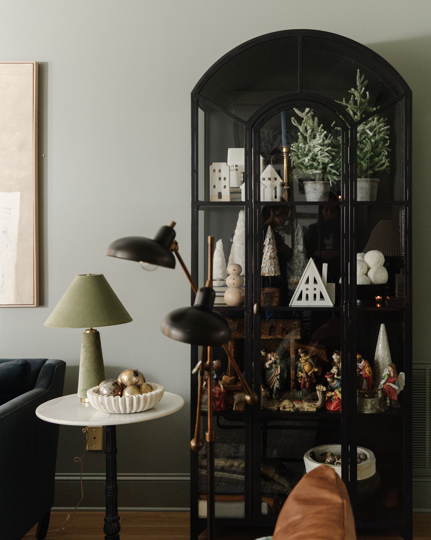 A sage green velvet lamp next to a standing console with Christmas decorations