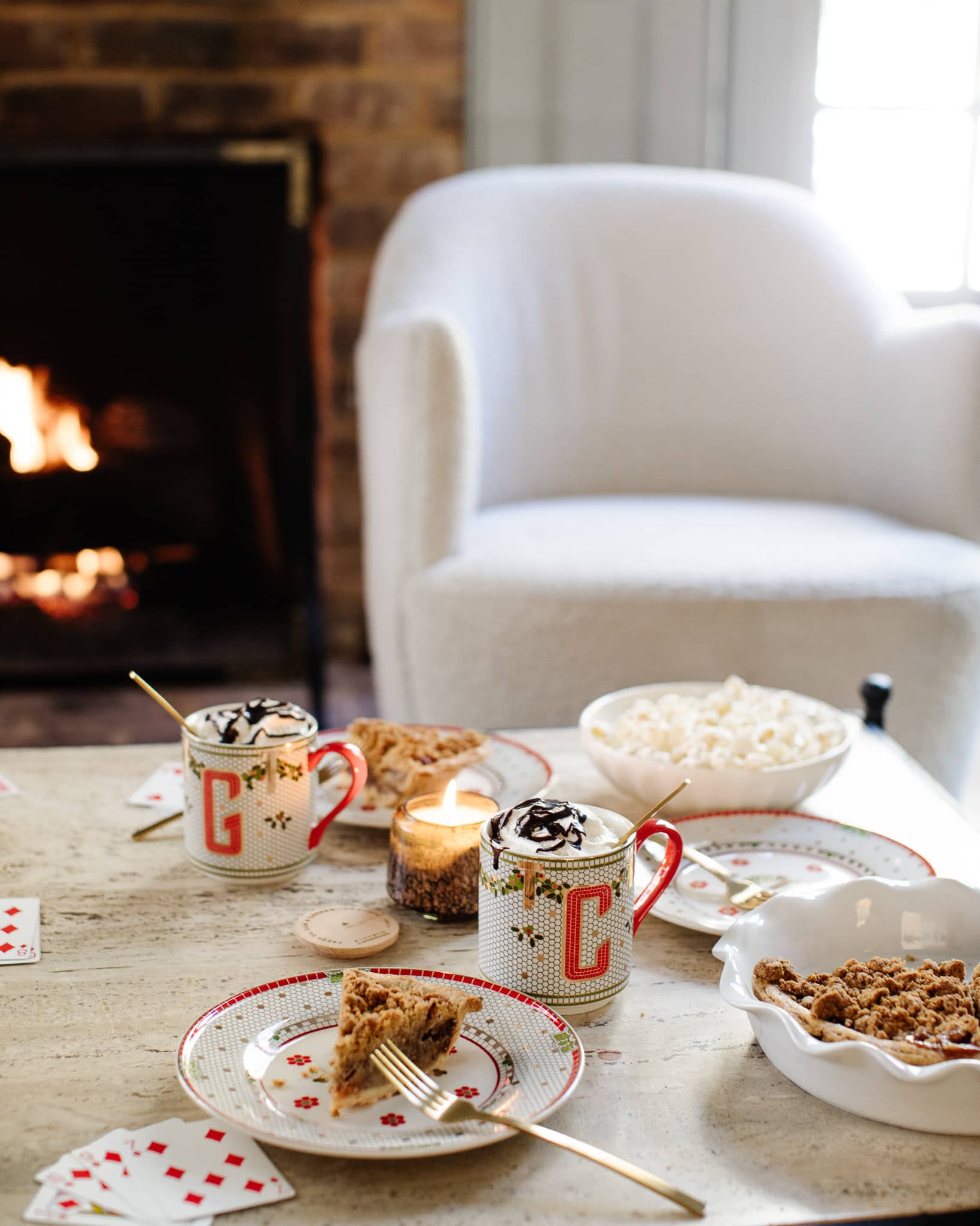 A coffee table with playing cards, popcorn, pie, and monogrammed mugs with hot cocoa and whipped cream