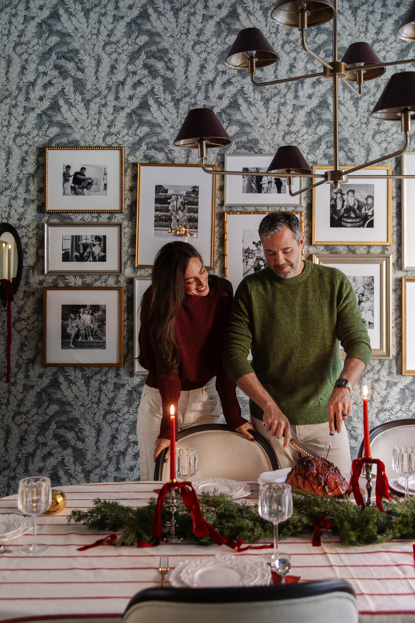 Chris and Julia standing at the dining room table and carving a ham for a festive dinner