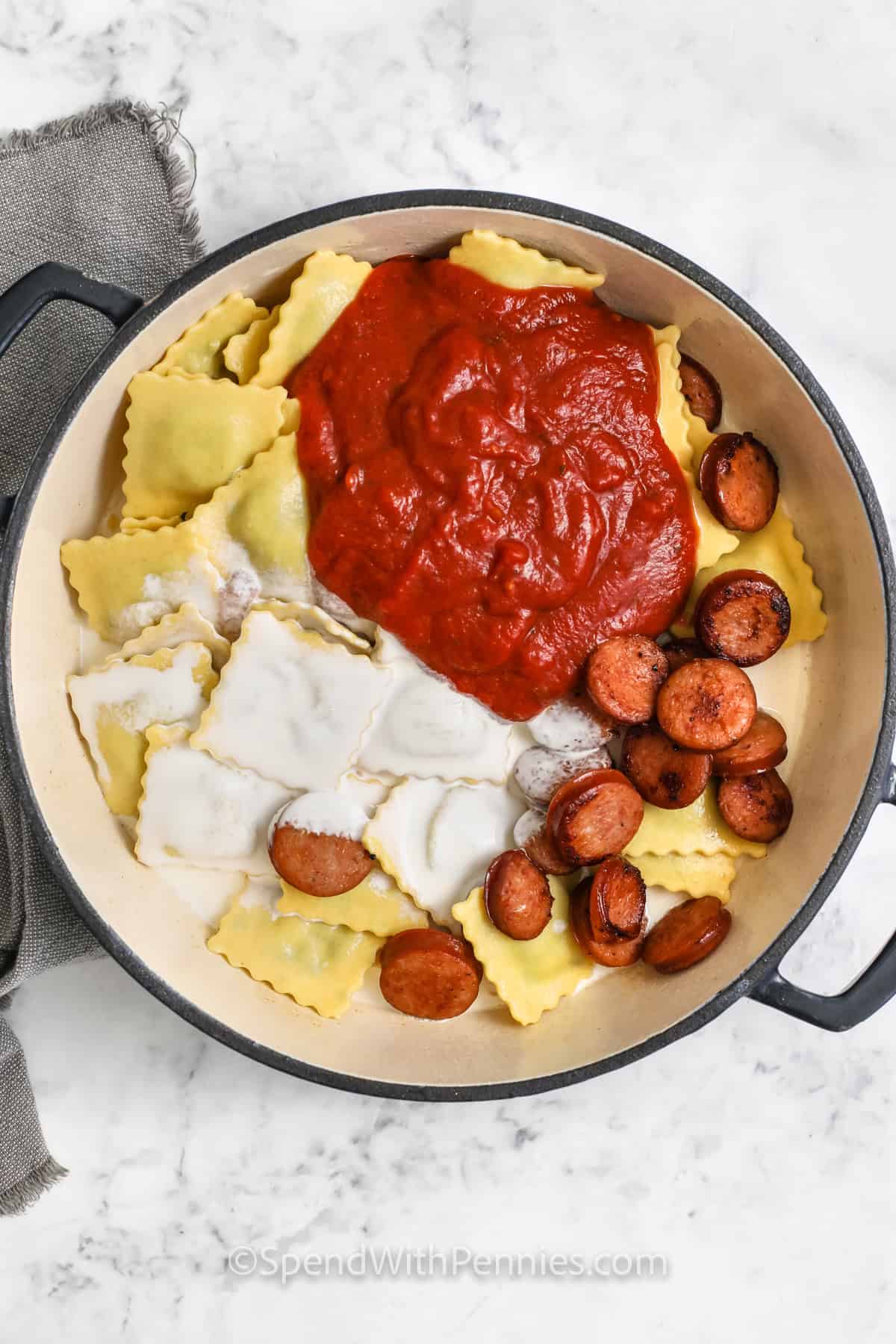 adding whipping cream and sauce to raviolis and sausage to make Easy Ravioli with Tomato Sauce