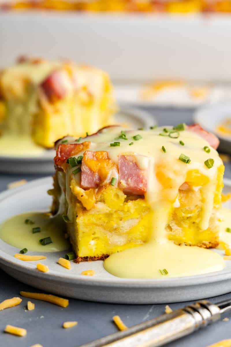 A single slice of eggs benedict casserole on a plate with hollandaise sauce drizzled over top.