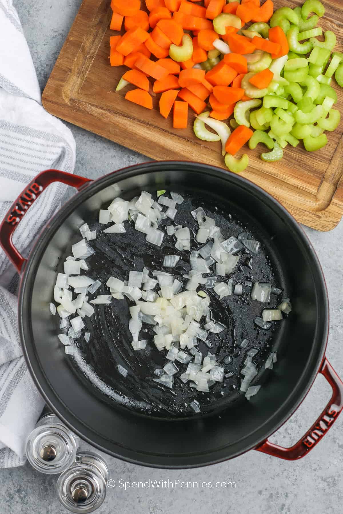 onions in a pot with carrots and celery on a wood board