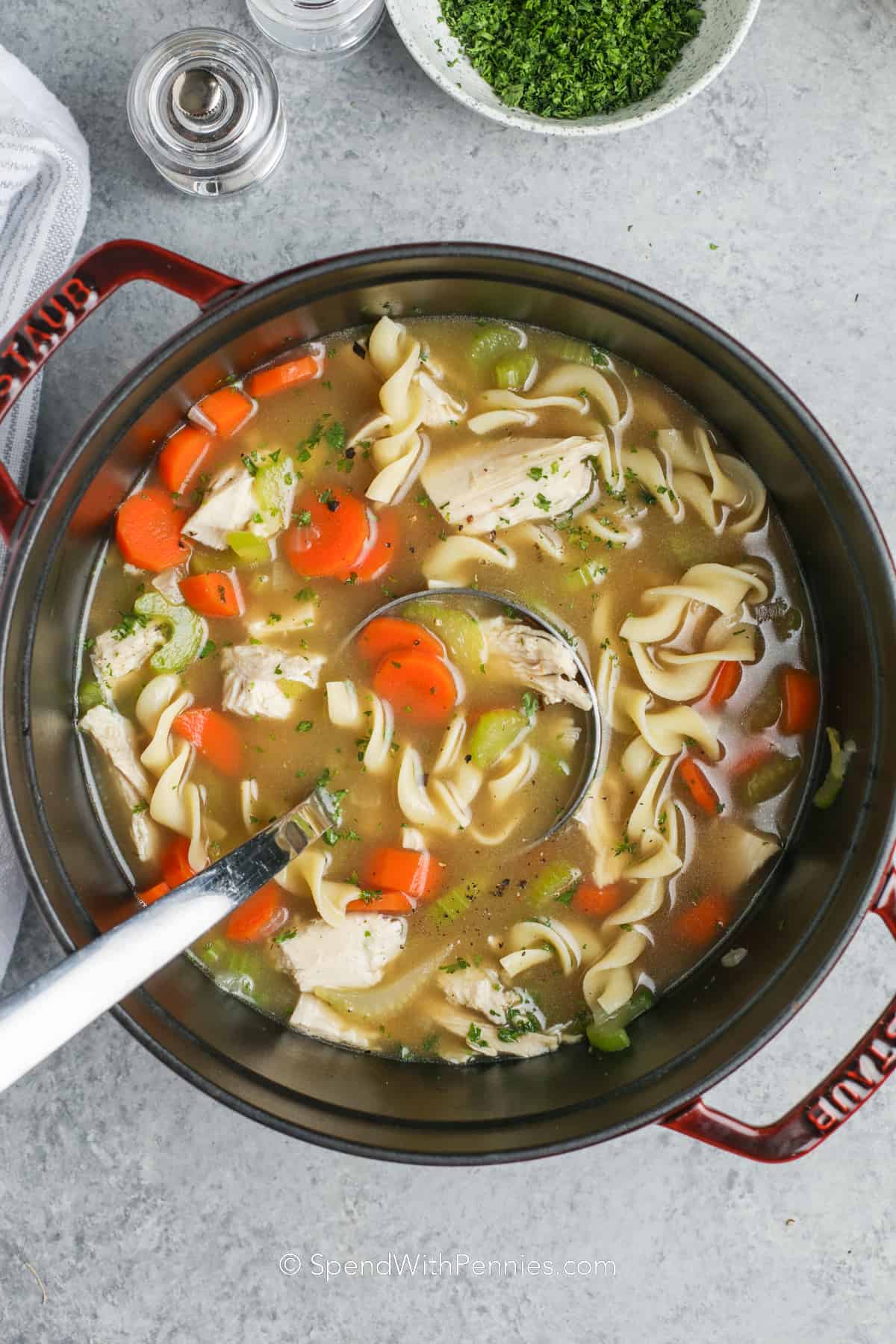 a pot of turkey noodle soup with a bowl of parsley