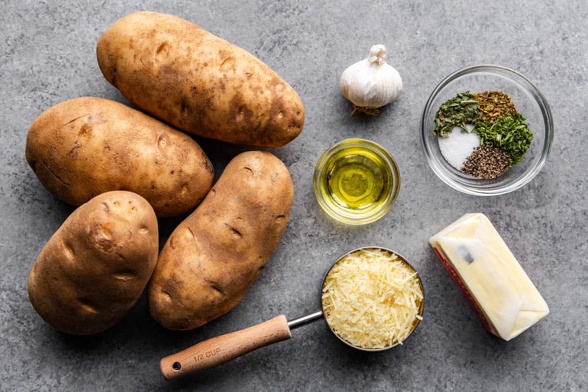 An overhead view of whole unpeeled potatoes and measured ingredients needed to make Garlic Herb Hasselback Potatoes.