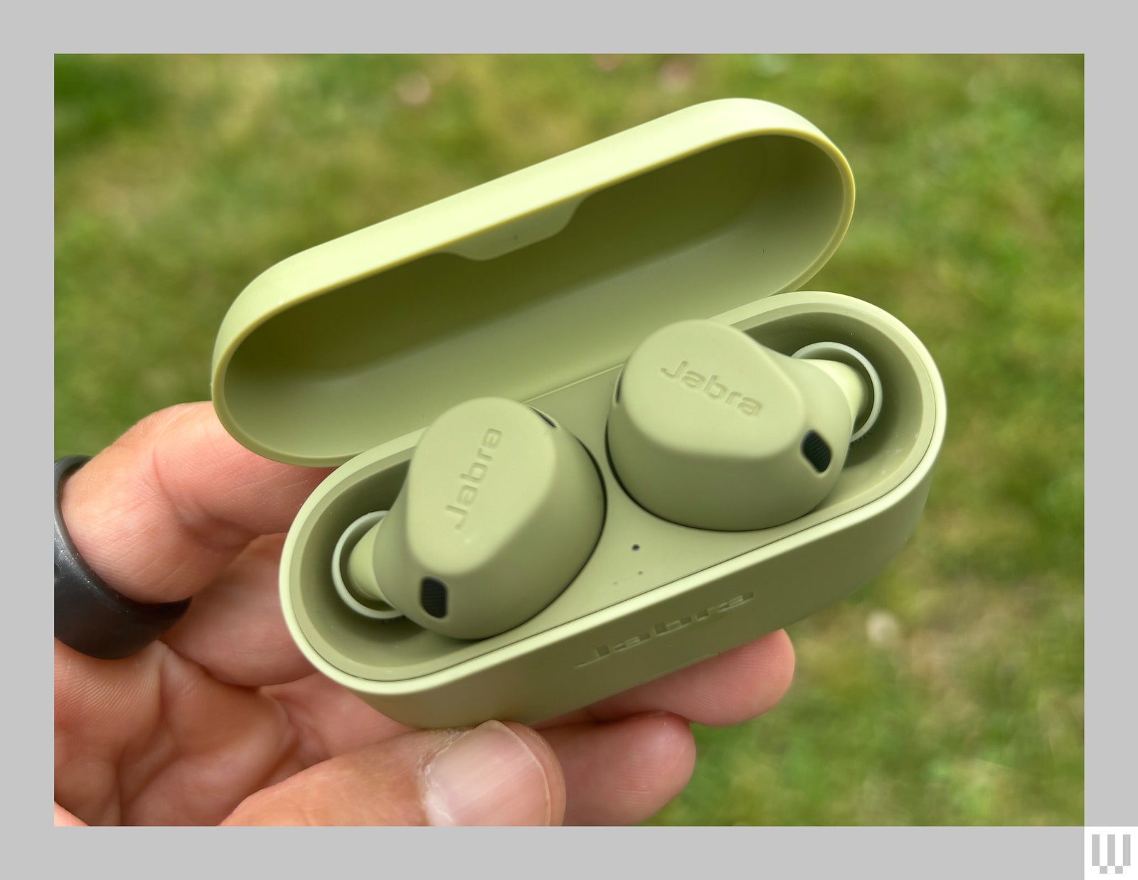 Hand holding a green ovalshaped case with 2 inear earbuds inside