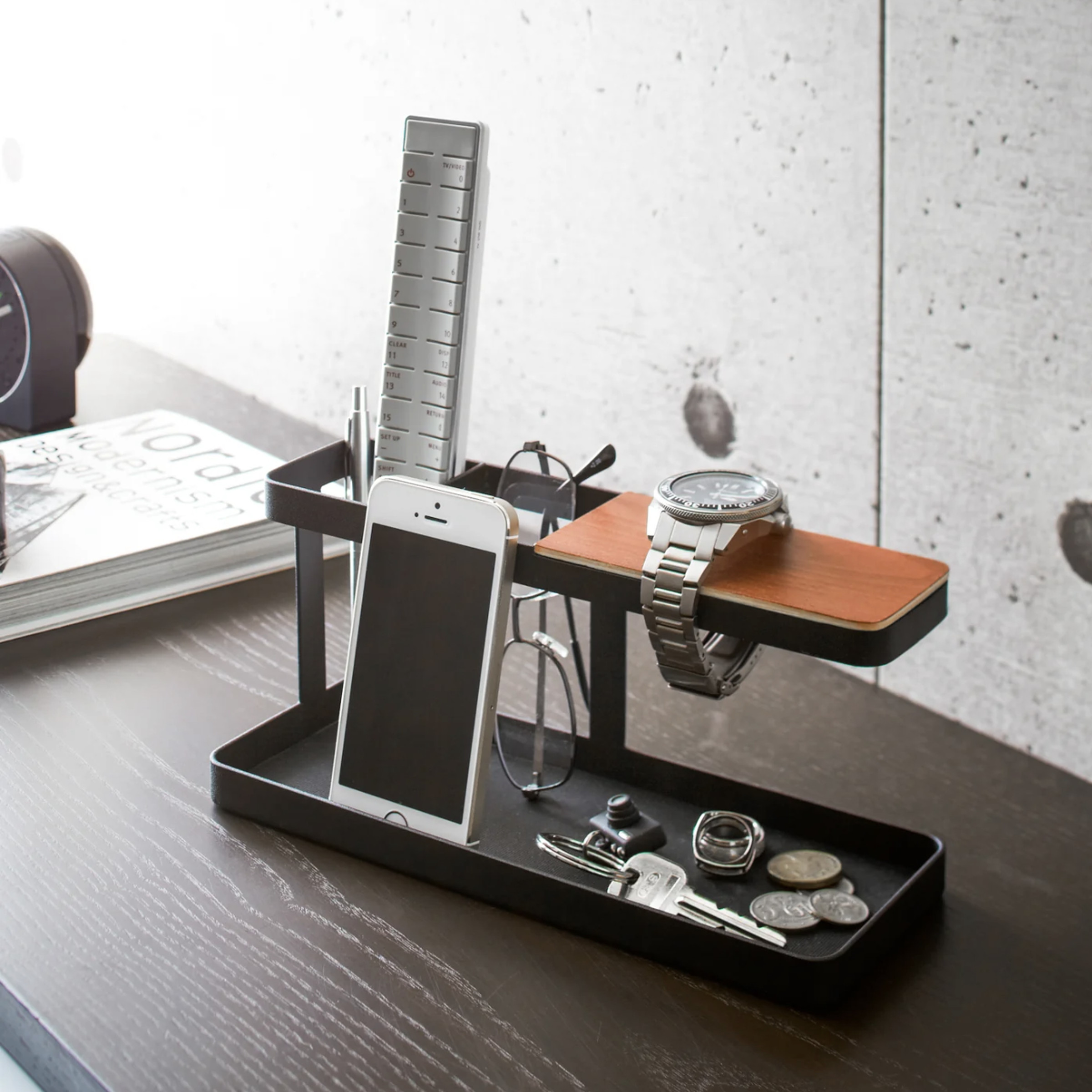 Black and brown two-level desk organizer loaded with small stuff like a phone, a watch, and a pair of glasses.