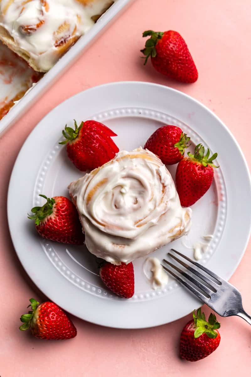 top view of strawberry roll covered in cream cheese on white plate