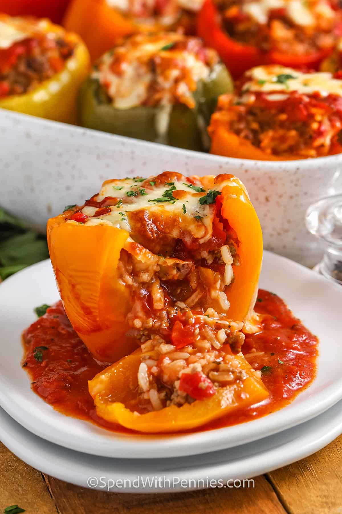 stuffed peppers on a plate sliced with baking dish of peppers in the background