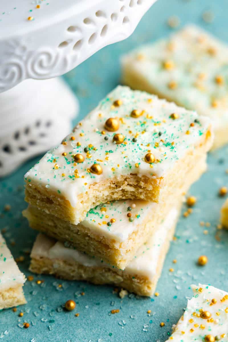 A stack of 3 sugar cookie bars with white frosting and sprinkles. The top bar has a bite taken out.