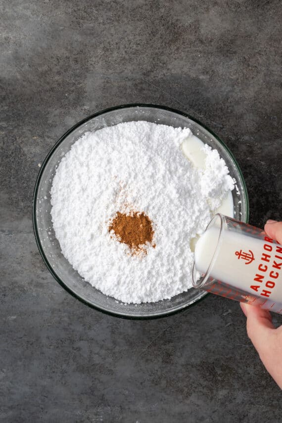 Pouring milk into a bowl of powdered sugar and ground nutmeg to make the icing.