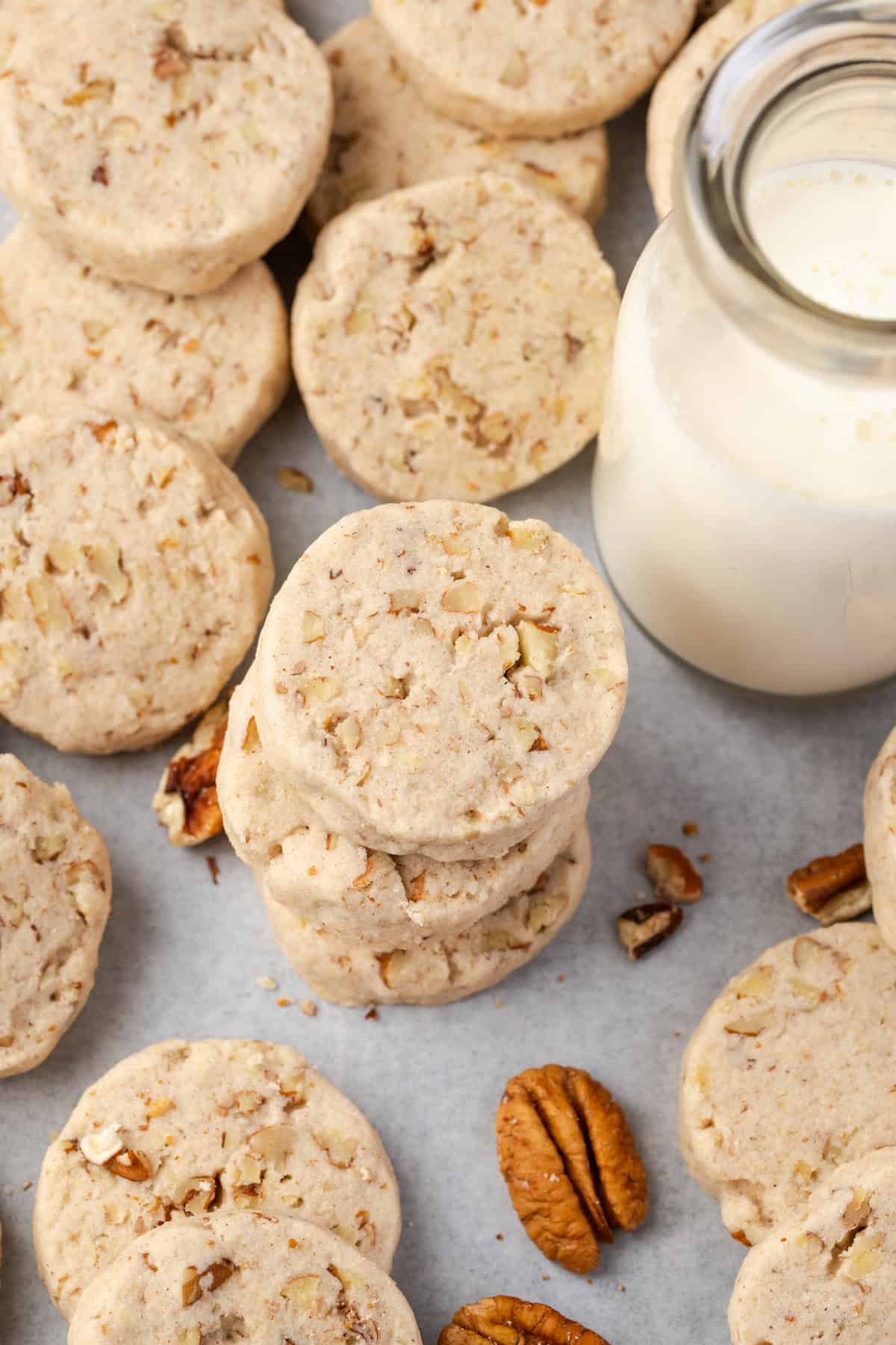 Overhead view of stacked pecan sandies surrounded by more scattered sandies next to a jug of milk.