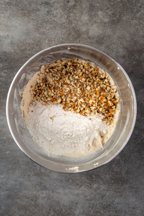 Dry ingredients added to pecan cookie dough in a metal bowl.