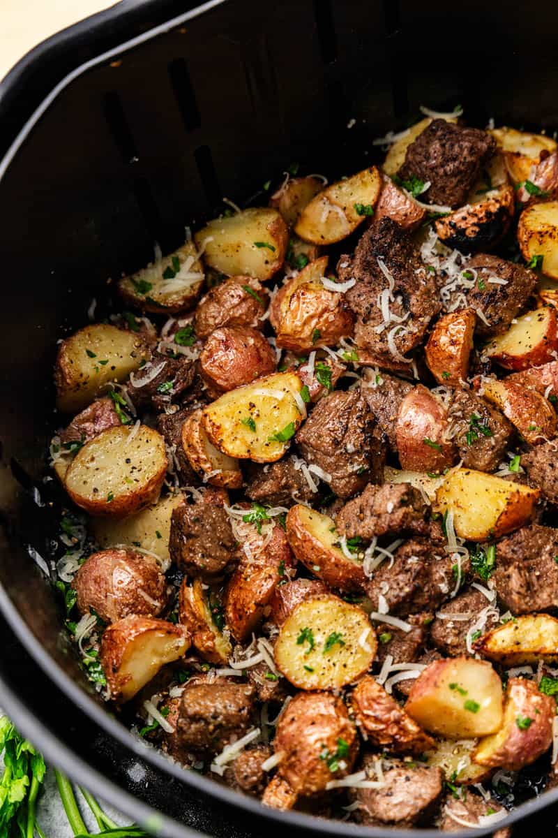 Steak bites and potatoes in the basket of an air fryer.