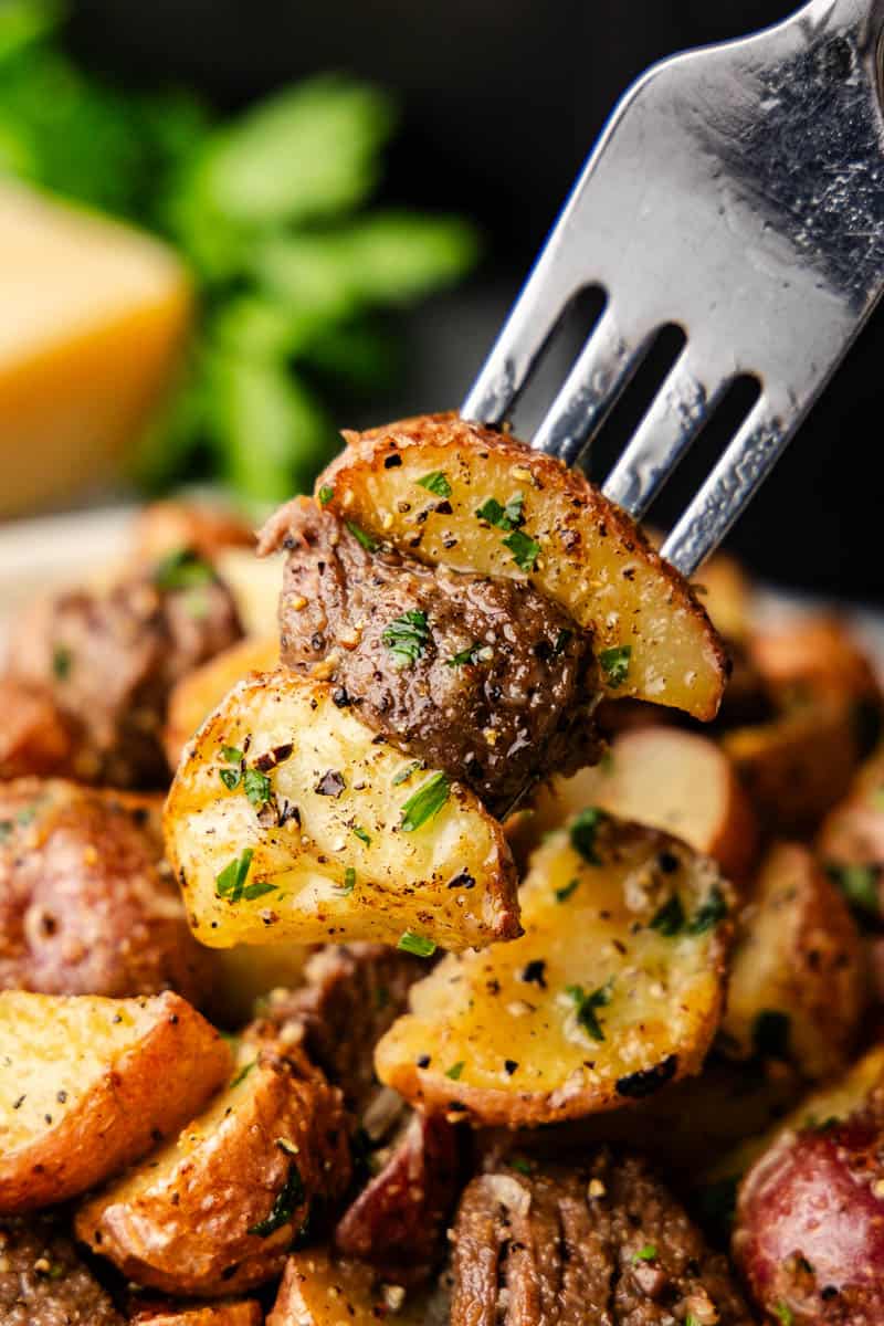 A super close up view of a fork lifting a bite of steak bites and potatoes from the plate.