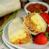 Breakfast burrito on a plate cut in half with strawberries on the side