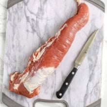 pork on a cutting board with a knife to show How to Remove Silverskin from Pork Tenderloin