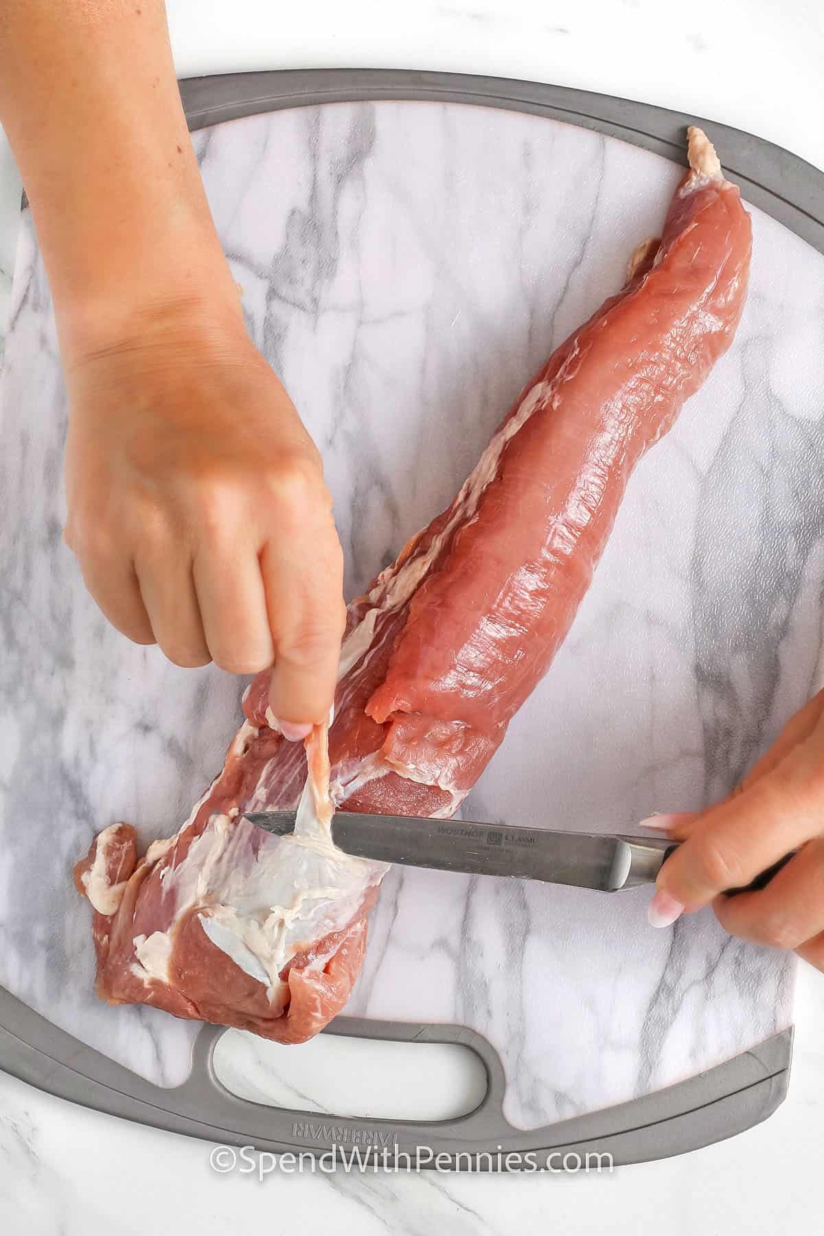 hands on a knife cutting pork to show How to Remove Silverskin from Pork Tenderloin