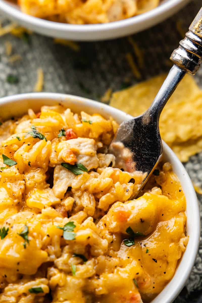 A close up view of a fork scooping out a bite of queso chicken and rice.